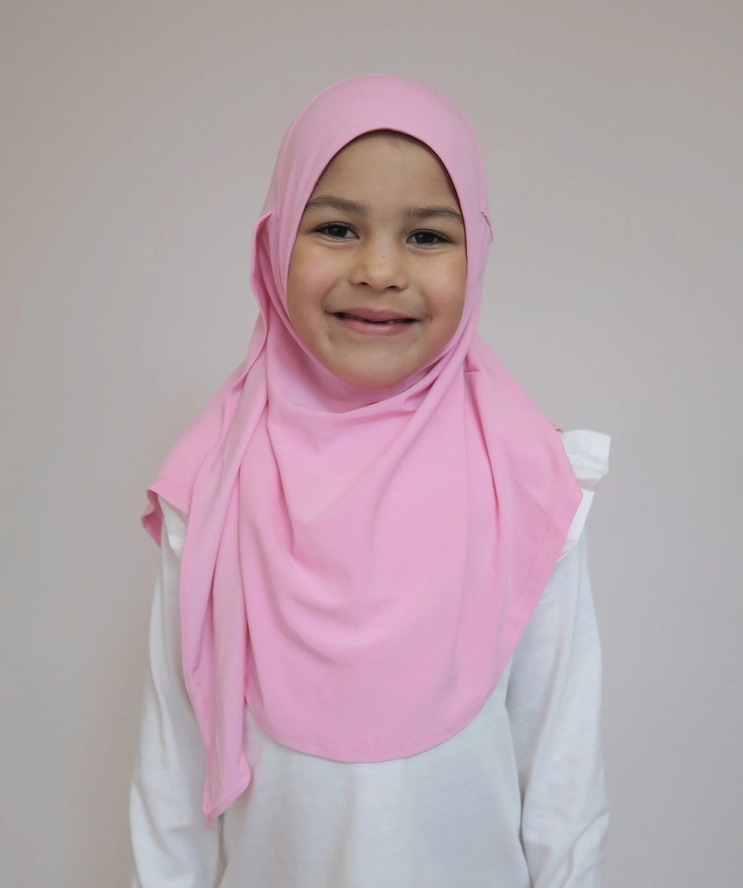 Child wearing a pink hijab and white shirt against a plain background