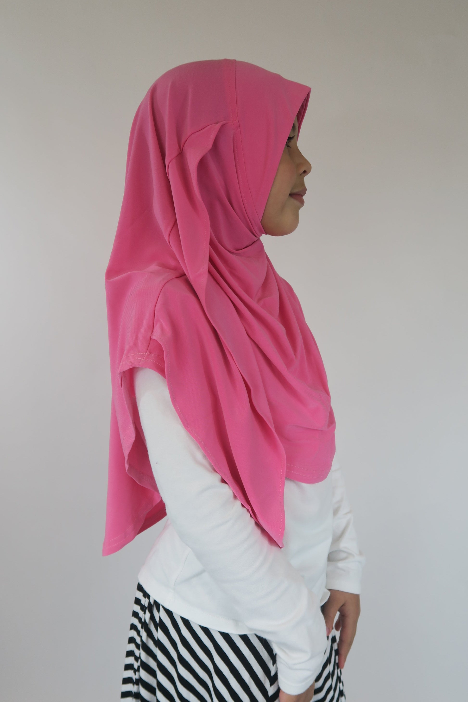 Person wearing a pink hijab and white outfit with black and white striped pants against a plain background