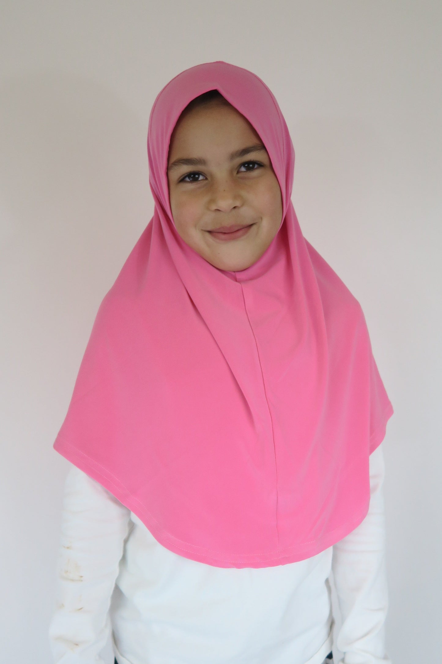 Person wearing a pink hijab and white outfit on a plain background