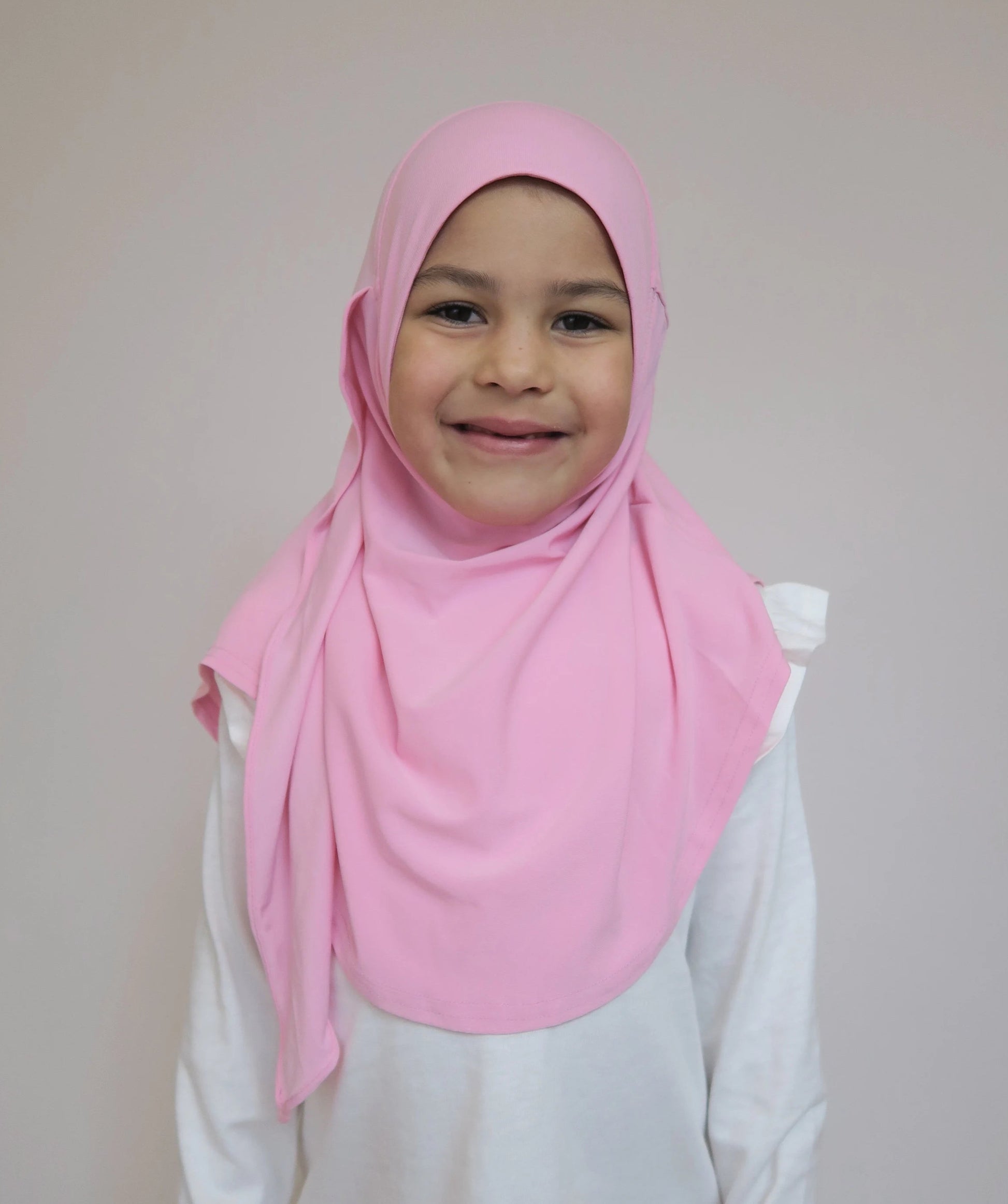 Child wearing a pink hijab and white shirt against a plain background